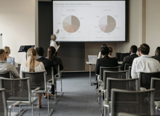 Woman Presenting Pie Charts to a Group of Coworkers